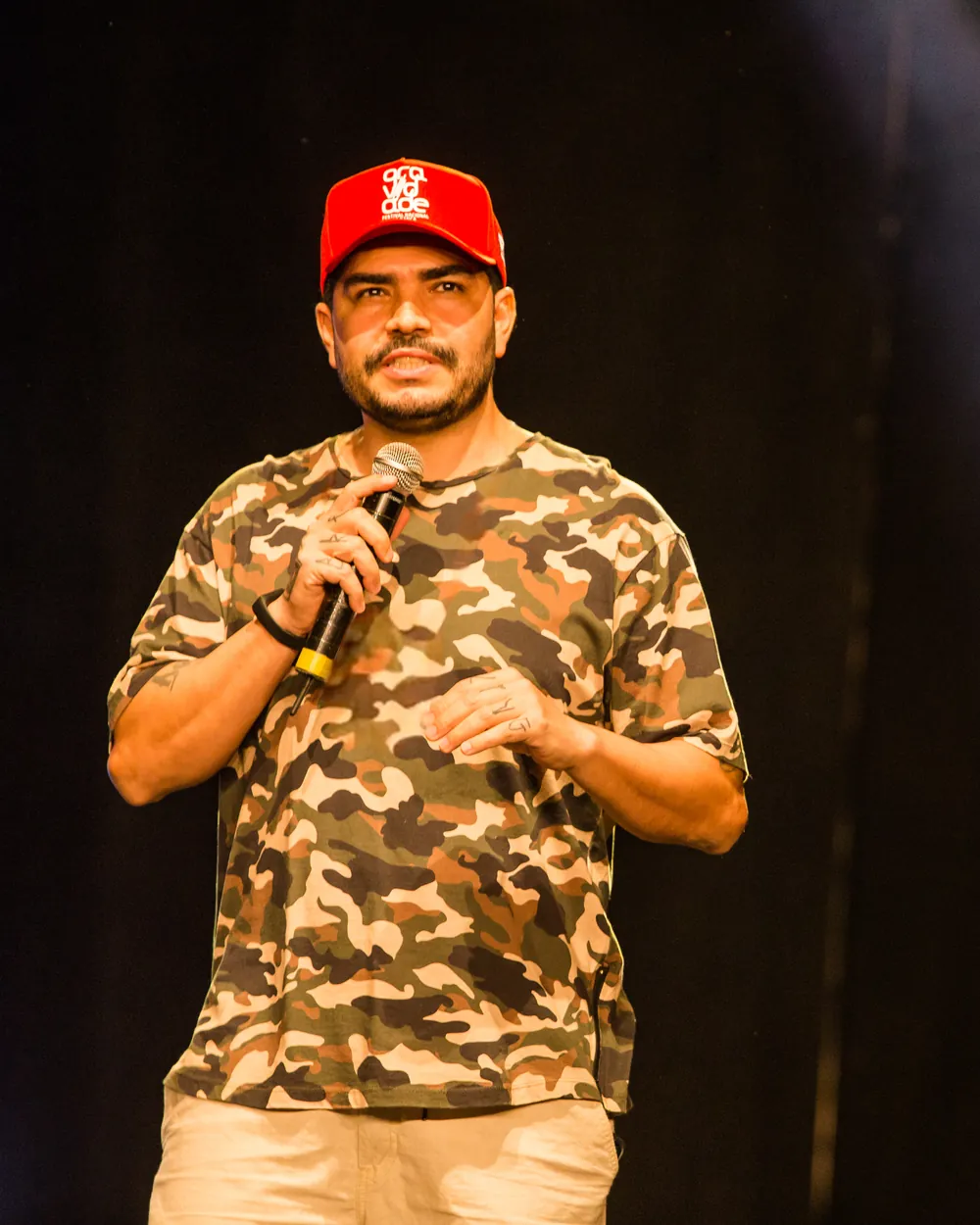 Ticko Bboy, palestrante da palestra O Marketing do Artista, com microfone e boné vermelho em palco em Votuporanga